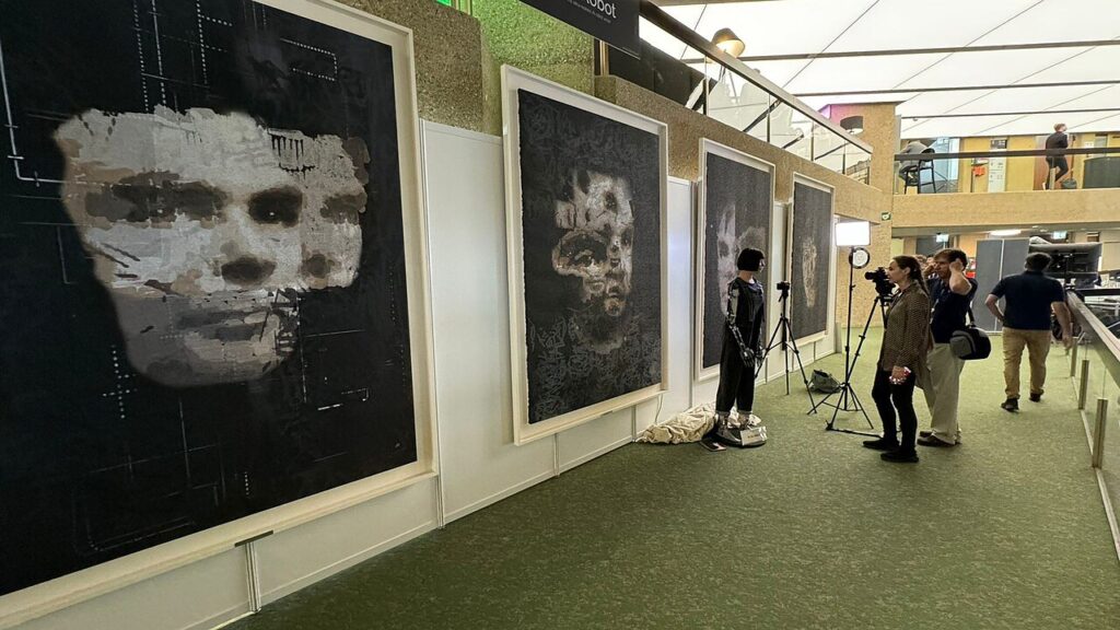 Il robot Ai-Da accanto ai suoi ritratti di Alan Turing